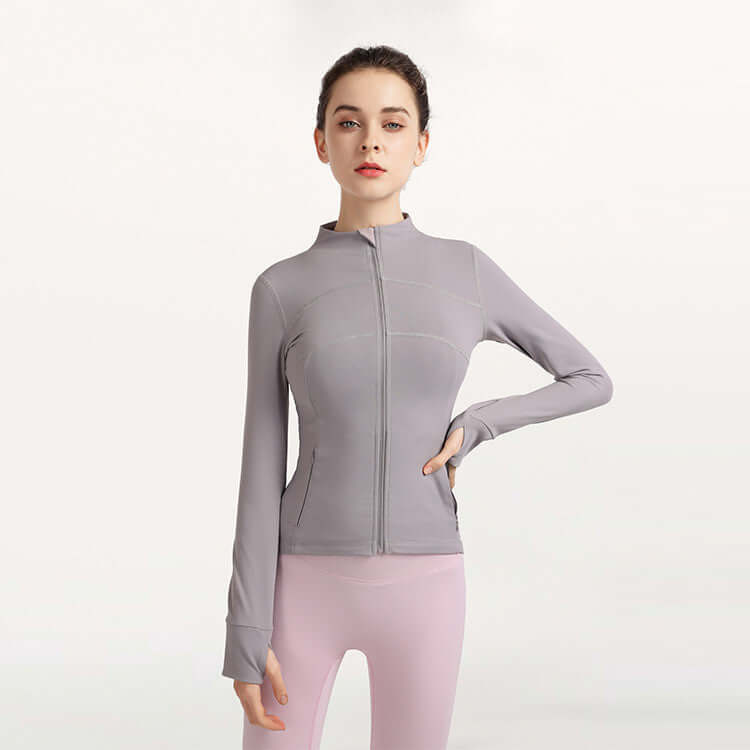 Woman wearing a gray zip-up jacket and pink leggings on a white background