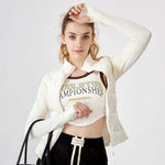 Woman wearing a white jacket and crop top with text, standing against a plain background