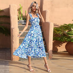 Woman in a blue floral dress standing outdoors with plants and stone steps in the background
