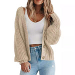 Women's thick knitted cardigan sweater in beige, warm button-down long sleeve, paired with a white crop top and blue jeans.
