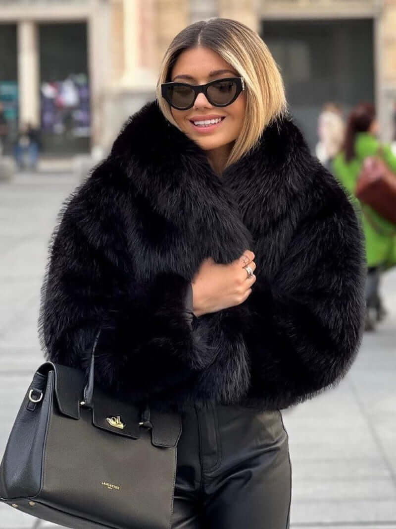 Woman wearing a stylish plush winter coat for women, smiling in a city setting, with sunglasses and a handbag.
